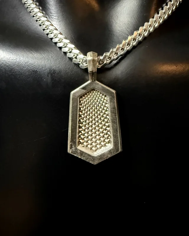 A hexagonal silver tag pendant with a dense pyramid stud field at its centre